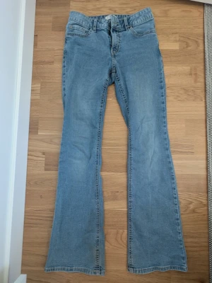 Ljusblå bootcut jeans med stjärndetaljer - Säljer ett par ljusblå bootcut jeans med snygga stjärndetaljer på bakfickorna och klassisk femficksdesign. Jeansen är normal till lågmidjade och är tillverkade i mjuk och lite stretchig denim. Perfekta för dig som gillar retrovibbar och vill ha ett par jeans som sticker ut lite extra. Jeansen är från Lindex i modellen "Freja". De är använda och har lite defekter längst ner på jeansen som man kan se på bild 5 men annars är de i ett bra skick. Säljer då de inte passar längre. Hör av er vid frågor💕