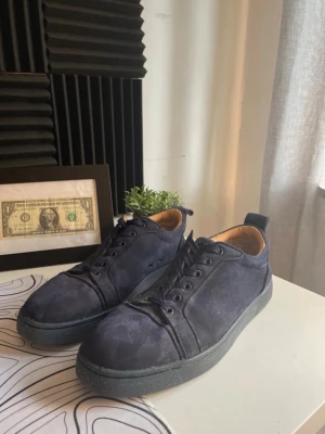 Mörkblå sneakers från Louboutin - Snygga mörkblå sneakers i mocka från Christian Louboutin med klassisk röd sula och diskret logga undertill. Lågt skaft och svarta snören ger en clean look. Perfekta för dig som vill ha något exklusivt och stilrent. Dem är använda ganska mycket men dem är helt äkta och jag har ej lådan pågrund jag har har haft dem länge!!!