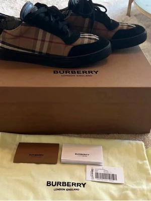 Burberry klassiska rutiga sneakers - Snygga sneakers från Burberry med det ikoniska beige-rutiga mönstret, svarta detaljer i läder och textil samt svarta skosnören. Låg modell med Burberry-logga på plösen. Perfekta för dig som vill ha en stilren och lyxig look. Skriv vid minsta fundering🙌🏼 vid en snabbaffär kan jag gå ner i pris