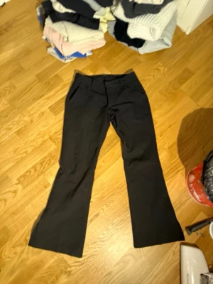 Svarta utsvängda kostymbyxor - Snygga svarta kostymbyxor med utsvängda ben och hög midja. Klassisk design med fickor fram och diskret gylf. Perfekta för en stilren look och passar till många olika outfits.