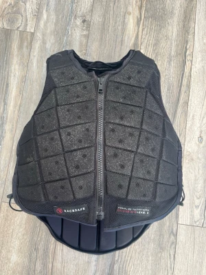 Racesafe väst - Säljer en svart skyddsväst från Racesafe, Level 3, med dragkedja framtill och ventilerande meshmaterial. Sparsamt använd så västen är i väldigt fint skick. St childs xl-long. Passat mig som är ca 168cm long och har st s.