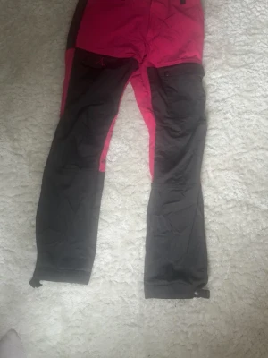 Byxor  - Storlek 160. snygg kombination av rosa och svart. Byxorna har förstärkta partier på knän och ben, praktiska fickor med knappar och justerbara benslut. Perfekta för vinterns alla äventyr och outdoor-aktiviteter. 