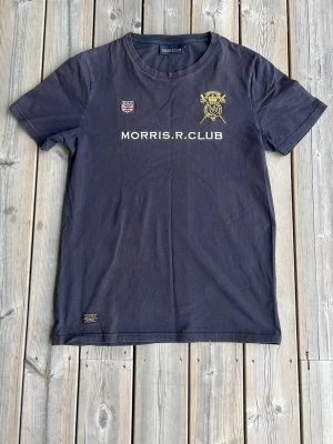 Morris marinblå t-shirt - Snygg marinblå t-shirt från Morris med tryck och broderade detaljer framtill. Klassisk rund hals och korta ärmar. Tillverkad i mjuk bomull som känns skön mot huden. Perfekt för dig som gillar stilrena plagg med sportig touch.