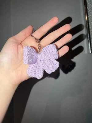 Ljuslila virkad nyckelring - Söt handgjord nyckelring med en virkad rosett i ljuslila bomullsgarn. Rosetten är mjuk och har en klassisk form, fäst i en metallkedja med ring.
