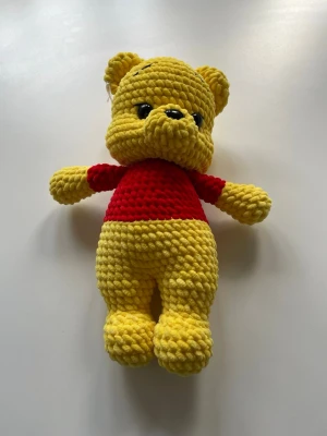 Gul stickad nallebjörn med röd tröja - Söt handgjord nallebjörn i mjukt, tjockt garn. Björnen är gul med en röd stickad tröja och har svarta ögon och nos. Perfekt som dekoration eller mysig present till någon som gillar gosedjur. Nalle puh inspirerad som är 31 cm