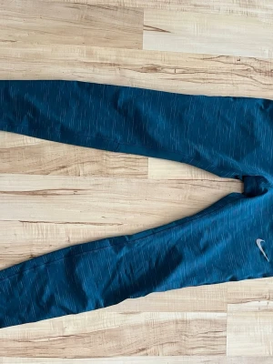 Blå Nike leggings med mönster - Snygga blå leggings från Nike med diskret mönster och logga på benet. De har en tight passform och bred midja för extra komfort. Perfekta för träning eller chill. Materialet är stretchigt och andas bra.
