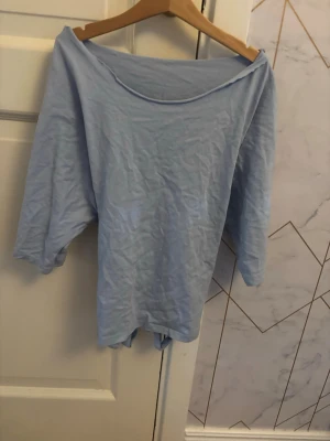 Ljusblå topp med knyt i ryggen - Ljusblå topp med trekvartsärm. Toppen har en snygg knyt-detalj i ryggen som ger en avslappnad och trendig look. Perfekt att styla med jeans eller kjol för en chill vibe.