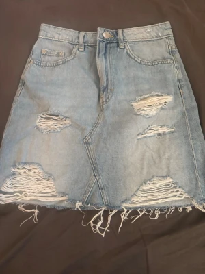 Ljusblå jeanskjol med slitningar - Trendig ljusblå jeanskjol med slitna detaljer och fransig nederkant. Perfekt för en avslappnad och cool stil.