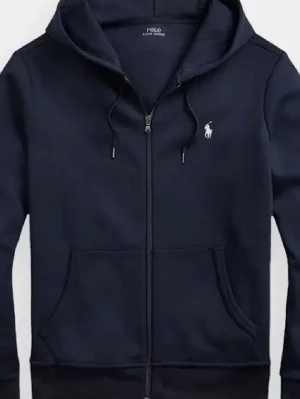 Marinblå hoodie från Polo Ralph Lauren - Snygg marinblå hoodie från Polo Ralph Lauren med dragkedja framtill, huva med dragsko och klassisk vit logga på bröstet. Tillverkad i mjuk bomullsblandning och har känguruficka. Perfekt för en avslappnad och stilren look.