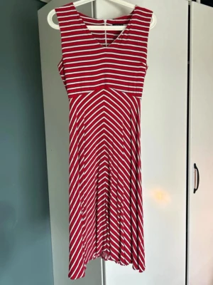 Röd och vit ärmlös randig klänning - Snygg ärmlös klänning med röda och vita ränder. Klänningen har v-ringning och mönstret skapar en cool effekt med diagonala och horisontella linjer. Perfekt för varma dagar och har en luftig passform som ger en avslappnad känsla.
