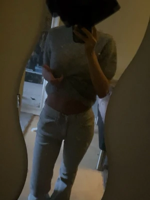 Grå stickad kortärmad tröja - Mysig grå stickad tröja med korta ärmar och rund hals. Tröjan har en enkel, klassisk design med ribbstickade muddar vid hals, ärmslut och nederkant. Perfekt att styla med jeans för en chill look.