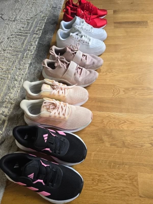Nike Adidas och Puma sneakers i olika färger - Paket pris för allt 700kr. Tre par sneakers: ett par helvita Nike Air Force 1 med klassisk design och perforerad tå, ett par ljusrosa Nike med bred kardborre och mesh-ovandel, samt ett par röda Puma sneakers med sportig look och snörning. Perfekta för dig som gillar streetstyle och färg.
