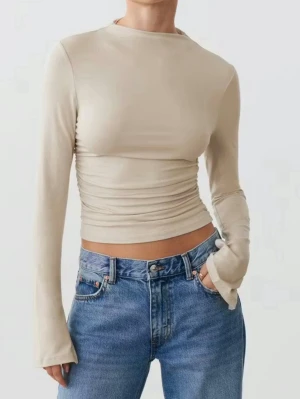 Beige croppad långärmad topp - Trendig beige croppad topp med långa ärmar och lätt rynkade sidor. Figurnära passform och slits vid ärmsluten. Tillverkad i mjukt material för en bekväm känsla. Toppen är från Gina Tricots Soft Touch serie