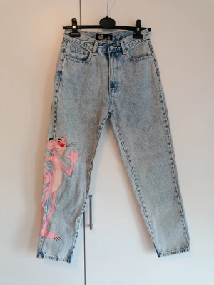 Ljusblå mom jeans med Pink Panther - Unika ljusblå mom jeans från Pull & Bear med hög midja och en stor tryckt Pink Panther-figur längs ena benet. Jeansen har klassisk femficksdesign och raka ben. Perfekta för dig som vill sticka ut med en cool och lekfull stil.