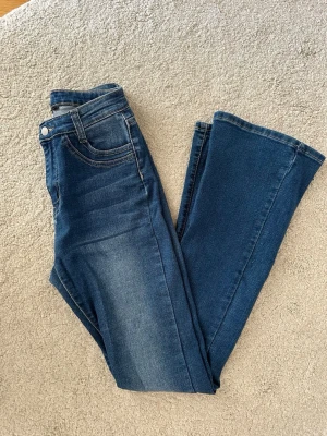 Blå bootcut jeans med hög midja - Snygga blå bootcut jeans med hög midja och klassiska fem fickor. Jeansen har en lätt tvättad look och utsvängda ben, perfekta för en trendig och avslappnad stil. Tillverkade i stretchigt denim för extra komfort.