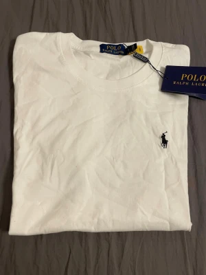 Vit t-shirt från Polo Ralph Lauren - Klassisk vit t-shirt från Polo Ralph Lauren med rund halsringning och korta ärmar. T-shirten har den ikoniska broderade loggan på bröstet och är tillverkad i mjuk bomull för en skön känsla. Perfekt basplagg med stilren design.
