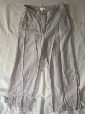Beige chinos från H&M, raka ben - Snygga beige chinos från H&M i storlek 40. Byxorna har raka ben, klassisk passform och stängs med knapp och dragkedja. Tillverkade i ett mjukt och lätt material som passar perfekt till en avslappnad stil. Fickor fram och bak för en clean look.
