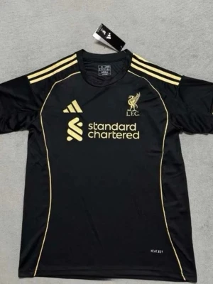 Svart Liverpool tränings t-shirt Adidas - Snygg svart tränings t-shirt från Adidas för Liverpool FC med gula detaljer och loggor. Tröjan har korta ärmar, rund hals och är tillverkad i ett lätt och ventilerande syntetmaterial. Perfekt för fotbollsträning eller sportiga aktiviteter.