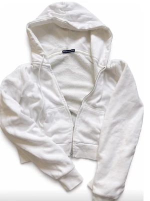 Vit cropped hoodie från Brandy Melville - Säljer en vit cropped hoodie från Brandy Melville med dragkedja framtill och två fickor. Hoodien har huva med snören och är tillverkad i mjukt bomullsmaterial. I storlek XS från Brandy Melville. 