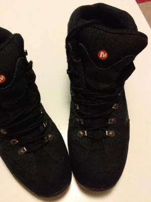 Merrell Kängor Svarta - Säljer robusta och bekväma vandringskängor från Merrell i mycket fint skick, väldigt lite använda och nästan som nya, med slitstark ovandel i textil/syntet med förstärkningar, stabil grovmönstrad sula med bra grepp för skog och terräng, vadderad insida för hög komfort samt klassisk snörning och bra stöd runt ankeln. Merrell vinterskor i storlek 45. Svarta kängor med hög skaftmodell och snörning framtill. Grovmönstrad yttersula för bättre grepp på snö och is.Passar som varma vinterskor för vardag
