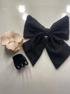 Set med håraccessoarer rosett & klämmor - Säljer ett set med tre håraccessoarer: en stor svart rosett i broderad spets, en beige hårklämma formad som en blomma och en liten svart hårklämma i plast. 