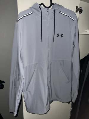 Under Armour Jacka - Snygg grå hoodie från Under Armour med dragkedja, svarta snören i huvan och logga på bröstet. Axelband med Under Armour-tryck och praktiska fickor framtill. Perfekt för en sportig och avslappnad stil. Super skick inga fläckar eller annat fel på den 9/10🌟