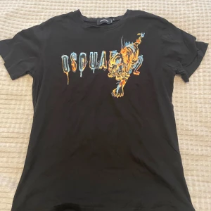 Svart Dsquared2 t-shirt med tigertryck - Cool svart t-shirt från Dsquared2 med färgstarkt tigertryck och droppande Dsquared2-logga på bröstet. T-shirten har rund hals och är tillverkad i mjuk bomull. Perfekt för dig som vill sticka ut med en unik och trendig look. Storlek XXL men sitter som L
