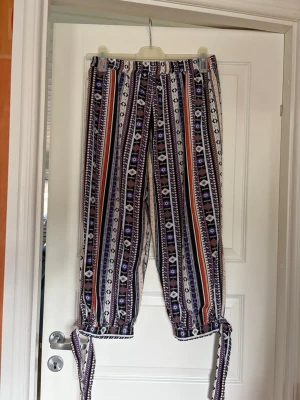 Mönstrade linnebyxor med knytband - Tunna byxor med färgglatt mönster i lila, svart, vitt och orange. Byxorna har raka ben och knytband vid bensluten för en cool det. Storlek XL, aldrig använda.