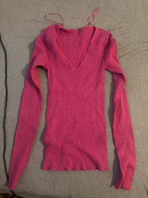 Rosa ribbstickad tröja  - Säljer en rosa ribbstickad tröja från Amisu med djup V-ringning och långa ärmar. Tröjan är figurnära och har en stretchig passform som sitter snyggt på kroppen. Perfekt för dig som gillar färg och vill ha något bekvämt och trendigt.