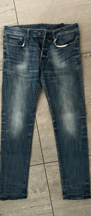 Blå slim fit jeans från G-Star RAW - Snygga blå slim fit jeans från G-Star RAW med slitna detaljer. Jeansen har en något tvättad look och smala ben. Storlek w:31 L32