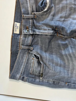 Grå slim fit jeans från Tiger of Sweden - Säljer ett par grå slim fit jeans från Tiger of Sweden med klassisk femficksdesign och orangea kontrastsömmar. Jeansen har normal midja och är tillverkade i mjuk denim med stretch för extra komfort. Hör gärna av dig vid frågor!