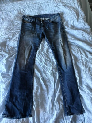Blå bootcut jeans med slitningar - Snygga blå bootcut jeans med lätt slitna detaljer och klassisk femficksdesign. Jeansen har en något utsvängd passform och kontrastsömmar. Perfekta för en avslappnad och trendig look.