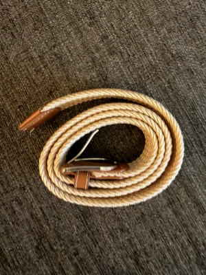 Grisch Beige flätat bälte  - Snyggt beige flätat bälte med bruna skinn-detaljer och silverfärgat spänne. Perfekt accessoar för att lyfta din outfit med en stilren och modern touch. Bältet är flexibelt, Grieg bälte och väldigt bra kvalité