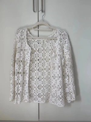 Vit virkad kofta med blommönster - Säljer en superfin vit virkad kofta med blommönster och långa ärmar. Koftan har en luftig och bohemisk känsla, perfekt att slänga över en topp. Tillverkad i mjukt garn och skulle gissa att den passar st M eller S