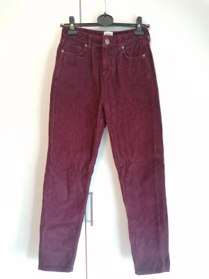 Vinröda raka manchesterbyxor - Snygga vinröda/plommonlila manchesterbyxor med raka ben och klassisk femficksmodell. Byxorna har hög midja och stängs med knapp och dragkedja. Tillverkade i mjuk manchester som ger en retrovibe och håller varmt. Stl W26, L32. 