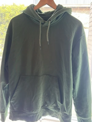 Grön hoodie från Jack & Jones - Mörkgrön hoodie från Jack & Jones med klassisk känguruficka och justerbar huva med dragsko. Tillverkad i mjuk bomullsmix och har ribbade muddar vid ärmslut och nederkant. Perfekt för en avslappnad och stilren look. Vill bli av med den därav pris 