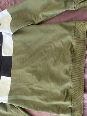Grön och svart sweatshirt från Lacoste - Snygg sweatshirt från Lacoste i grönt, svart och vitt med klassisk krokodillogga på bröstet. Tröjan har långa ärmar, rund halsringning och är gjord i mjukt bomullsmaterial. Perfekt för en avslappnad och trendig stil.