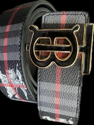 Burberry rutigt skärp med B-spänne - Säljer ett snyggt rutigt skärp från Burberry med ett stort B-formad spänne i svart och guld. Skärpet har klassiskt Burberry-mönster i svart, grått och rött samt en cool detalj med en vit häst. Perfekt för att lyfta din outfit.