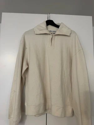 Krämvit stickad tröja från Zara - Säljer en krämvit stickad tröja från Zara med halv dragkedja och bred krage. Tröjan har ribbade muddar och är tillverkad i ett mjukt, tjockt material som passar perfekt för kyligare dagar. Enkel och stilren design som är lätt att matcha.