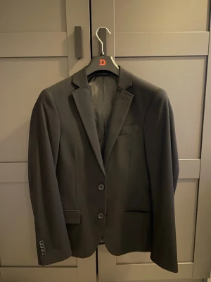 Svart kostym med kavaj och byxor - Perfekt tillfälle att köpa en snygg svart kostym med klassisk kavaj och matchande byxor, super bra inför studenten eller balen. Kavajen har två knappar framtill, smala slag och fickor med lock. Byxorna har pressveck och bakficka med knapp. Perfekt för dig som vill ha en stilren och tidlös look. ⚠️Kostymen har endast  används en gång under fjolårets bal och har sen dess hänt fint och prydligt i garderoben.😄 Kavajen är i storlek S42 och byxorna i w27 l30, exakta mått kan skickas efter förfrågan.