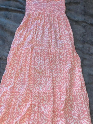 Rosa och vit långkjol mönstrad - Säljer en söt långklänning från Kappahl i rosa och vitt med ett mönster som påminner om batik. Klänningen har smock upptill och är ärmlös, perfekt för varma dagar. Tillverkad i mjuk bomull som känns skön mot huden.