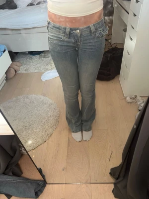 Blå true religon bootcut jeans med broderade fickor - Säljer ett par blå bootcut jeans ifrån true religon med snygg tvätt och broderade detaljer på bakfickorna. Jeansen har låg midja och klassisk femficksmodell. 