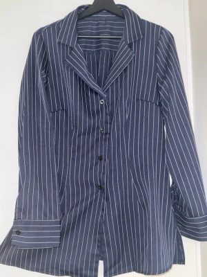 Blåvit randig skjorta med knappar - Snygg blå skjorta med vita ränder och klassisk krage. Skjortan har långa ärmar, knäppning framtill och en relaxed passform. Perfekt för en stilren look och enkel att matcha med jeans eller kostymbyxor.