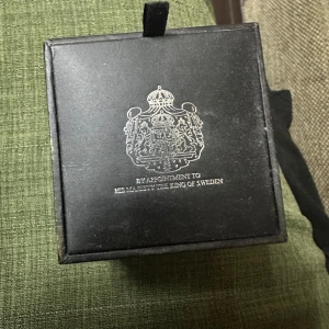Blå manschettknappar The Lion - Snygga manschettknappar med blå bakgrund och ett vitt lejonmotiv. Runda och silverpläterade, perfekta för att ge skjortan en kunglig touch. Kommer i originalask med svensk kunglig hovleverantörslogga. Klassisk och stilren accessoar.
