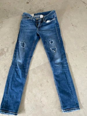 Blå slitna jeans från Dondup - Säljer ett par blå jeans från Dondup med slitningar och hål på benen. Hör av er vid frågor eller prisförslag 