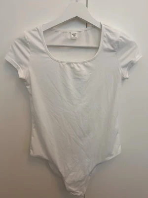 Vit basic body med kort ärm - Enkel och stilren vit body från Shein med korta ärmar och rundad urringning. Tillverkad i mjukt stretchigt material som sitter skönt mot kroppen. Perfekt att matcha med jeans eller kjol för en clean look.