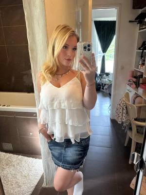 Vit volangig linnetopp - Säljer en superfin vit linnetopp med tunna axelband och flera lager volanger. Toppen har v-ringning och är tillverkad i ett lätt, luftigt material som passar perfekt till sommaren. Enkel att styla med jeanskjol eller shorts. Aldrig använd!