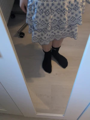 Vit kjol med blått blommönster - Kort, volangig kjol i vitt med blått blommönster och dekorativa kanter. Kjolen har en luftig passform och dubbla volanger som ger en söt och somrig look. Perfekt för dig som gillar romantisk och bohemisk stil. Inte använd så mycket, fråga gärna efter mer info! Är 158/164 men passar Xs/S