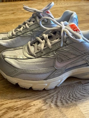 Grå Nike sneakers med vit sula - Snygga grå sneakers från Nike med vit sula och klassisk swoosh på sidan. Skorna har mesh- och syntetpaneler för extra komfort och andningsförmåga. Lågt skaft och snörning framtill. Perfekta för en sportig och trendig look. Använd fåtal gånger pga för stora för mig men returdatumet har löpt ut.