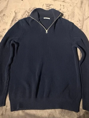 Marinblå halvzip  - Mörkblå stickad tröja från Zara med halvzip och hög krage. Tröjan har ribbad struktur, långa ärmar och breda muddar vid ärmslut och nederkant. Perfekt för lager på lager och en clean look.